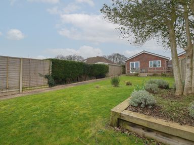 A backyard with grass a wooden raised garden bed and a pathway leading to a brick house at The Lobster Pot in Overstrand