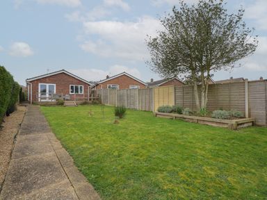 A backyard with a lawn a paved walkway a tree and a wooden fence surrounding houses at The Lobster Pot in Overstrand
