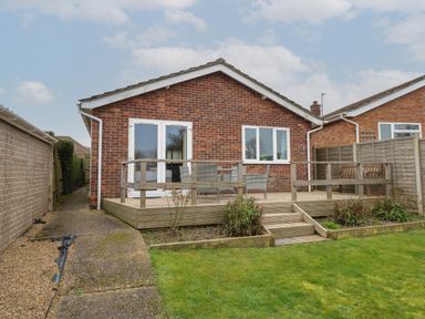 A backyard with a raised wooden deck with chairs and a table and a grass lawn at The Lobster Pot in Overstrand