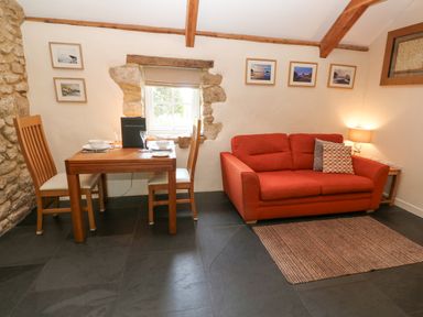 A room with a red sofa a small wooden dining table with two chairs and framed pictures on the wall at Godolphin Barn in Ashton near Rosudgeon