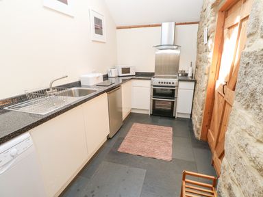 A kitchen with white cabinets a stainless steel oven a wooden door and stone walls at Godolphin Barn in Ashton near Rosudgeon