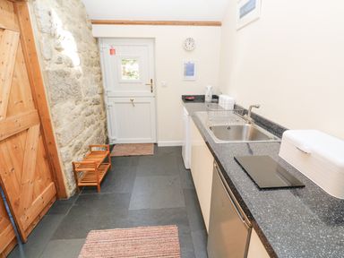 A kitchen with a stone wall wooden door white door sink countertop and rugs at Godolphin Barn in Ashton near Rosudgeon
