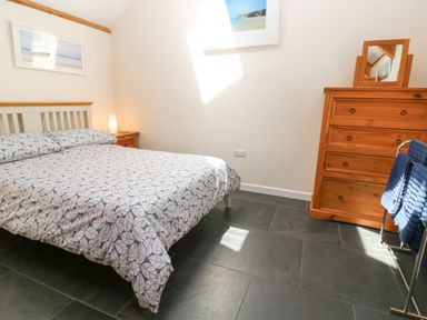 A bedroom with a bed a wooden chest of drawers and a towel rack at Godolphin Barn in Ashton near Rosudgeon