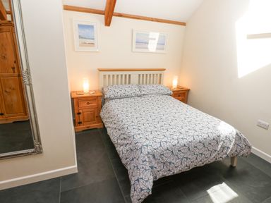 A bedroom with a bed and patterned bedspread two wooden bedside tables with lamps and framed pictures on the wall at Godolphin Barn in Ashton near Rosudgeon