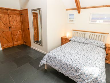 A bedroom with a bed with patterned bedding wooden bedside tables with lamps wooden doors and a wall mirror at Godolphin Barn in Ashton near Rosudgeon