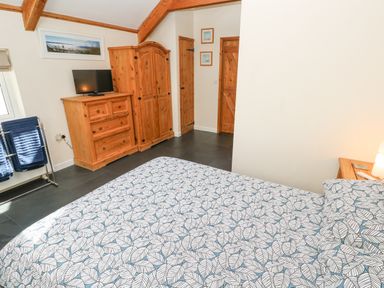 A bedroom with patterned bedspread wooden wardrobe chest of drawers and a small television at Godolphin Barn in Ashton near Rosudgeon