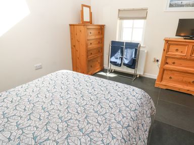 A bedroom with a bed covered in leaf patterned bedding wooden dressers a towel rack with towels and a window at Godolphin Barn Ashton near Rosudgeon