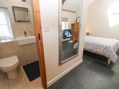 A bathroom with a toilet and sink next to a bedroom with a bed a chest of drawers and a large mirror on the wall at Godolphin Barn in Ashton near Rosudgeon