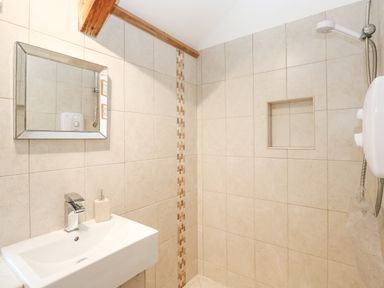 A bathroom with a wall-mounted sink a mirror a showerhead and tiled walls at Godolphin Barn in Ashton near Rosudgeon