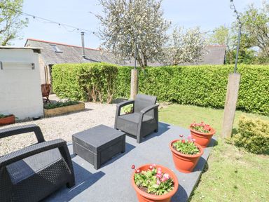 A garden patio with black outdoor chairs and table and potted flowers at Godolphin Barn in Ashton near Rosudgeon