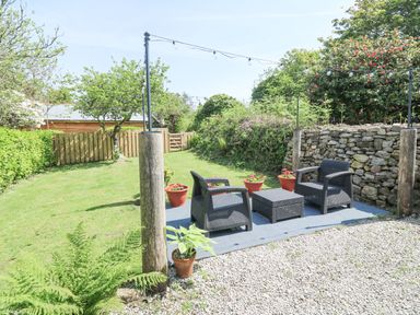 An outdoor seating area with two chairs and a table on a rug surrounded by flower pots and a stone wall at Godolphin Barn Ashton near Rosudgeon