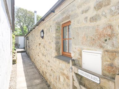 A stone exterior wall with a wooden window and gate labeled Godolphin Barn in Ashton near Rosudgeon