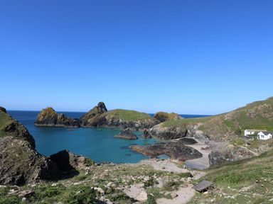 A coastal landscape with rocky cliffs green grass and a small beach near two white houses at Godolphin Barn in Ashton near Rosudgeon