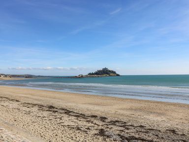 A sandy beach with calm sea waves and an island with a castle in the distance at Godolphin Barn in Ashton near Rosudgeon