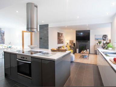 A modern kitchen with an island and oven next to a living area with a sofa and TV at Hafod Heli in Rhosneigr