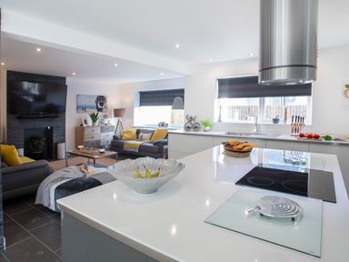 A modern kitchen and living area with white countertops a fruit bowl a TV and sofas at Hafod Heli in Rhosneigr