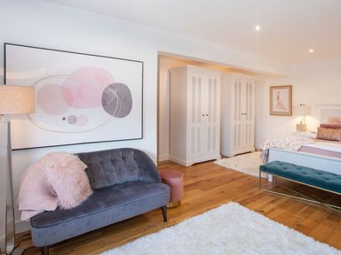 A bedroom with a gray sofa and white wardrobes on wooden floor at Hafod Heli in Rhosneigr