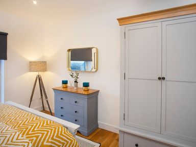 A bedroom with a grey wardrobe a blue chest of drawers a lamp and a bed with a yellow patterned blanket at Hafod Heli in Rhosneigr