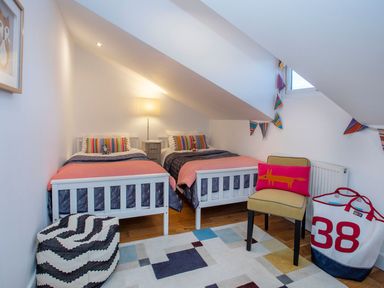 A bedroom with two beds a lamp a chair and a large bag at Hafod Heli in Rhosneigr