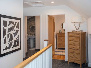 A hallway with a wooden chest of drawers and lamp next to two open doors showing a bathroom and a room with another chest of drawers at Hafod Heli in Rhosneigr
