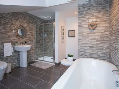 A bathroom with a bathtub a shower enclosure a pedestal sink a toilet and a small stool with a plant at Hafod Heli in Rhosneigr