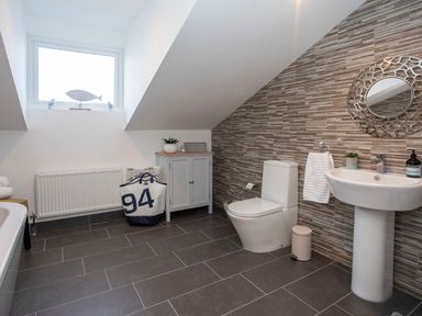 A bathroom with a toilet sink cabinet and a laundry bag at Hafod Heli in Rhosneigr