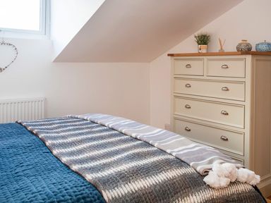 A bedroom with a bed covered in blue and gray blankets and a white chest of drawers with decorative items at Hafod Heli in Rhosneigr