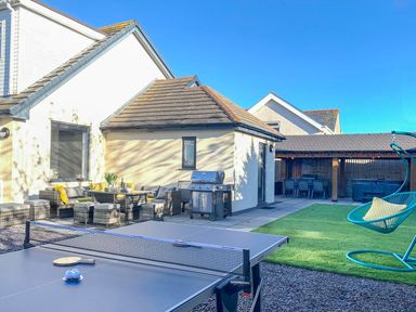 An outdoor patio with a ping pong table seating area grill and hanging chair at Hafod Heli in Rhosneigr