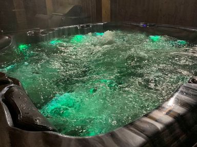A bubbling hot tub with green lights in a wooden indoor setting at Hafod Heli in Rhosneigr