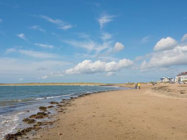 A sandy beach with seaweed by the shore people walking near buildings in the distance at Hafod Heli in Rhosneigr