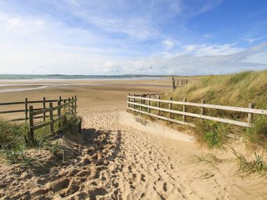 A sandy pathway with wooden fences leading to a beach with dunes and the sea in the background at Hafod Heli in Rhosneigr