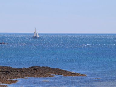 A sailboat and a small motorboat on the sea near a rocky shoreline at Hafod Heli in Rhosneigr