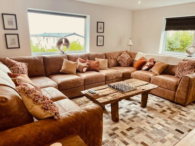 A living room with a large brown sectional sofa and a wooden coffee table with a chess set at Hafod Heli in Rhosneigr