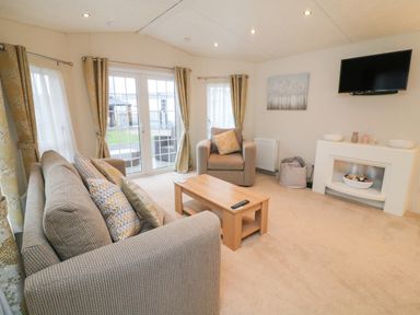 A living room with a sofa a chair coffee table television and glass doors at The Bobbin Number 11 South Lakeland Leisure Village near Carnforth