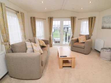 A living room with a sofa armchair coffee table and windows with curtains at The Bobbin Number 11 South Lakeland Leisure Village near Carnforth