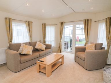 A living room with a sofa armchair coffee table and windows with curtains at The Bobbin Number 11 South Lakeland Leisure Village near Carnforth