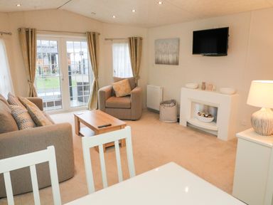 A living room with sofa armchair coffee table wall mounted TV and sliding glass doors at The Bobbin Number 11 South Lakeland Leisure Village near Carnforth