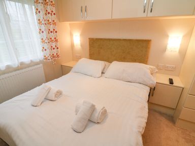 A bedroom with a double bed with white bedding and rolled towels on the bed at The Bobbin Number 11 South Lakeland Leisure Village near Carnforth