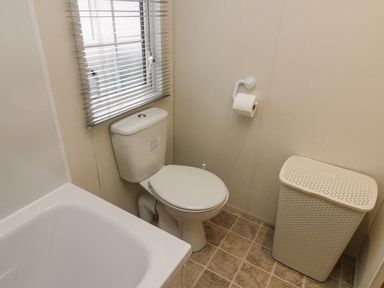 A bathroom with a toilet a bathtub a window with blinds a toilet paper holder and a laundry basket at The Bobbin Number 11 South Lakeland Leisure Village near Carnforth