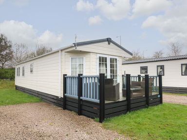 An exterior view of a beige static caravan with a small patio area with chairs and glass railing at The Bobbin Number 11 South Lakeland Leisure Village near Carnforth