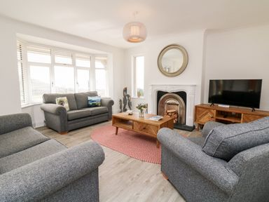A living room with gray sofas a wooden coffee table a round rug a fireplace and a television at Greenbank in Woolacombe