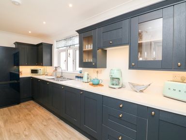 A kitchen with dark cabinets light countertop appliances and a window at Greenbank in Woolacombe