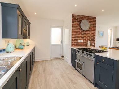 A kitchen with dark cabinets, a stove, brick wall with a clock, and mint green appliances at Greenbank in Woolacombe