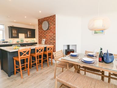 A kitchen with a breakfast bar and wooden stools next to a dining table with wicker chairs and place settings at Greenbank in Woolacombe