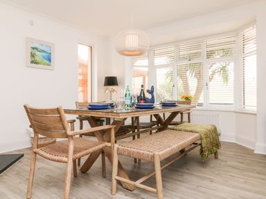 A dining area with a wooden table and chairs next to a window with blinds at Greenbank in Woolacombe