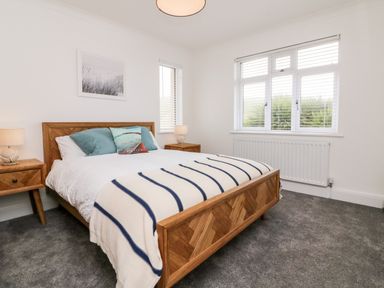 A bedroom with a wooden bed frame and bedside tables with lamps next to a window with blinds at Greenbank in Woolacombe