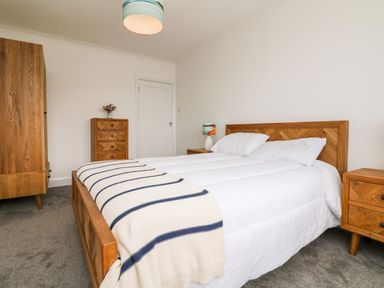 A bedroom with a wooden bed frame a white bedspread and pillows wooden bedside tables a chest of drawers and a wardrobe at Greenbank in Woolacombe