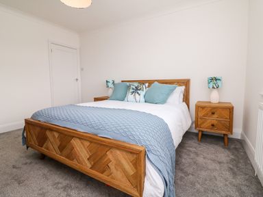A bedroom with a wooden bed frame two bedside tables with lamps and blue and palm tree pillows at Greenbank in Woolacombe