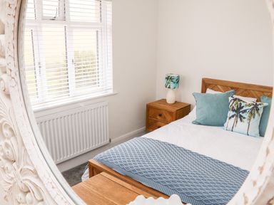 A bedroom with a wooden bed white bedding blue pillows a wooden bedside table with a lamp and a window with blinds at Greenbank in Woolacombe