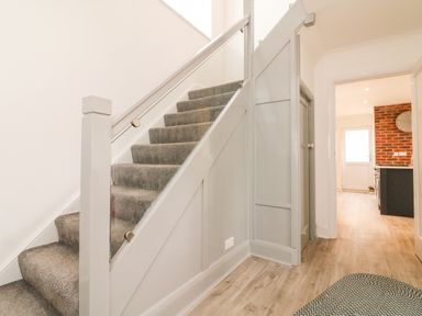 A hallway with carpeted stairs and wooden flooring leading to a kitchen with exposed brick walls at Greenbank in Woolacombe
